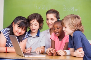 Interracial primary classroom learning to use laptop with their teacher.