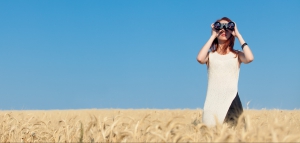 Redhead girl in white dress with binocular at wheat field.